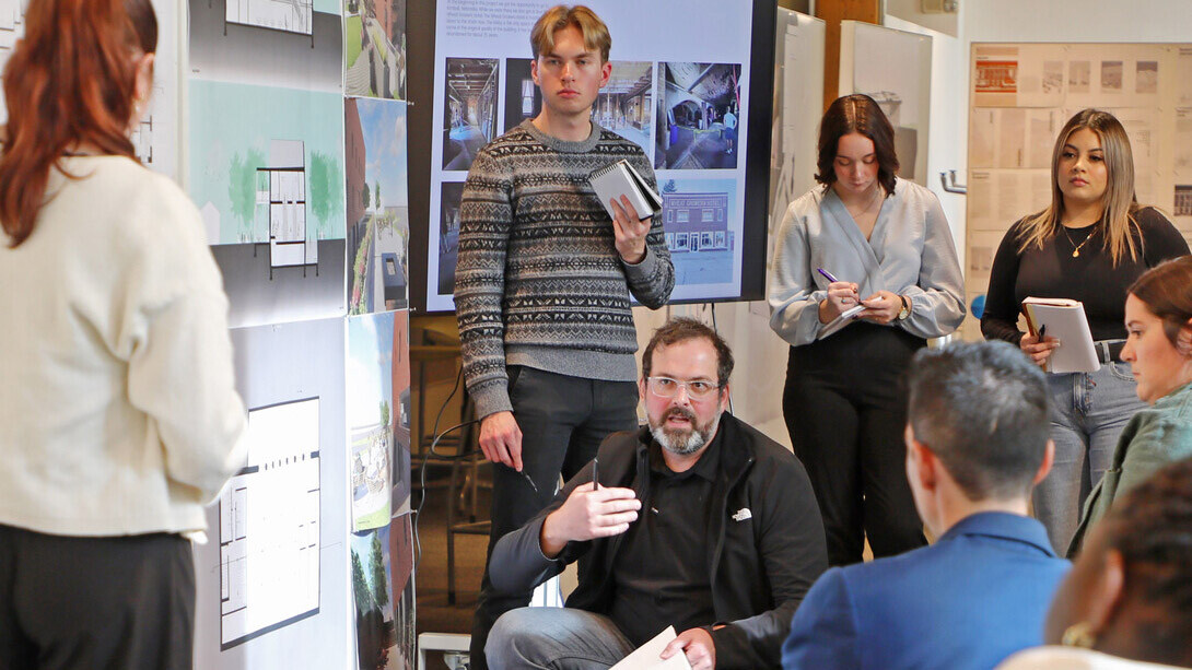 Nate Bicak (center), associate professor of interior design, speaks to a group of seven students in a classroom.