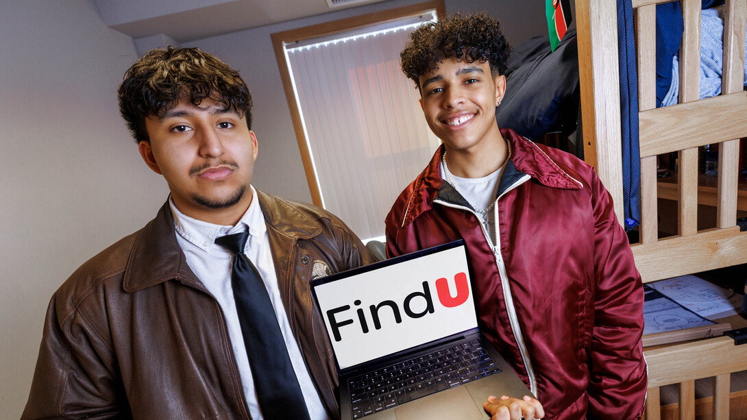 Raikes School students Kenny Morales (left), a software engineering major, and Wilson Overfield, a computer science major, hold a laptop displaying the FindU logo in their dorm room.