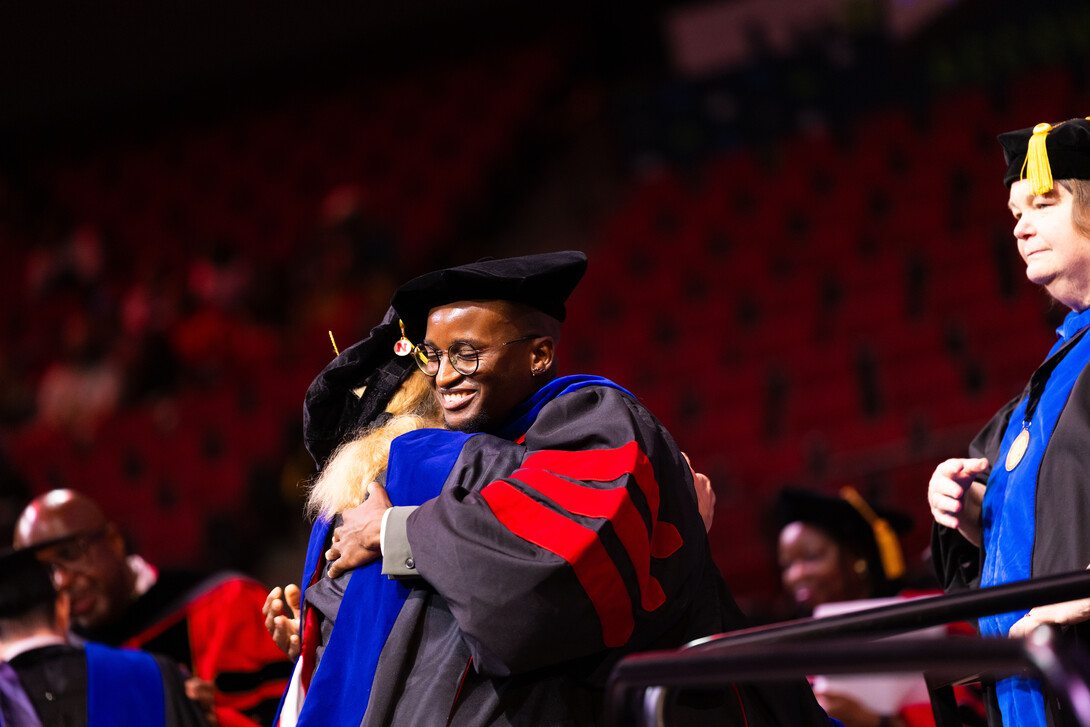 Esihle Lupindo hugs his adviser, Lisa Kort-Butler, after receiving his doctoral hood during the combined graduate and undergraduate commencement ceremony Aug. 16 at Pinnacle Bank Arena.