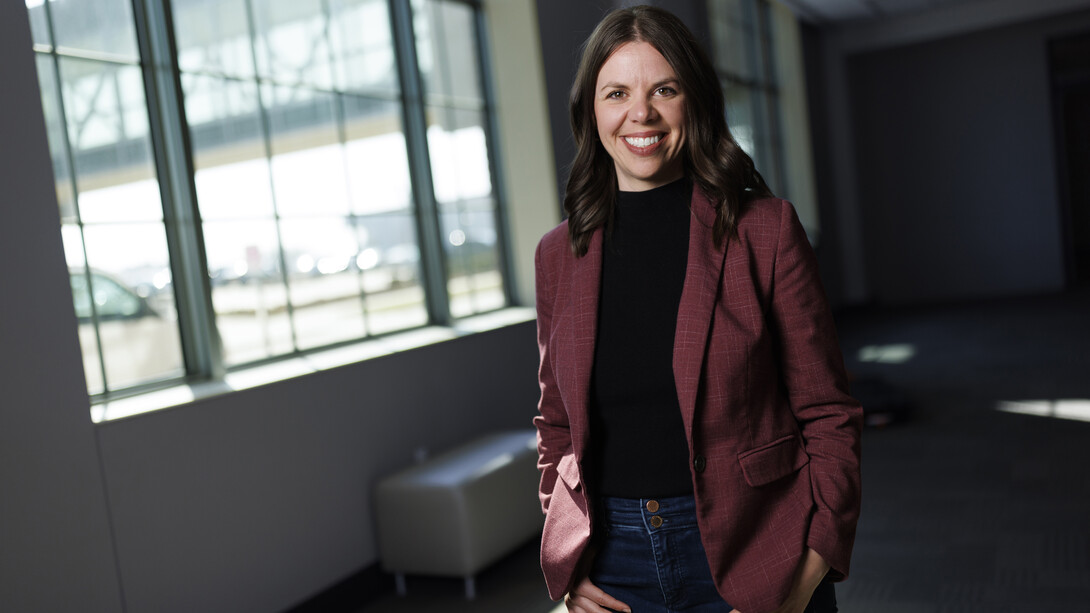Jordyn Bader, Husker alumna and cofounder of Marble Technologies, smiles as she stands next to a window in a shadowy corridor.