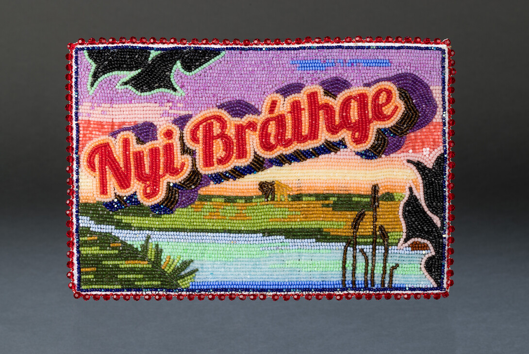 A colorful beaded work of a landscape with the words "Nyi Bráthge" in red letters on top.