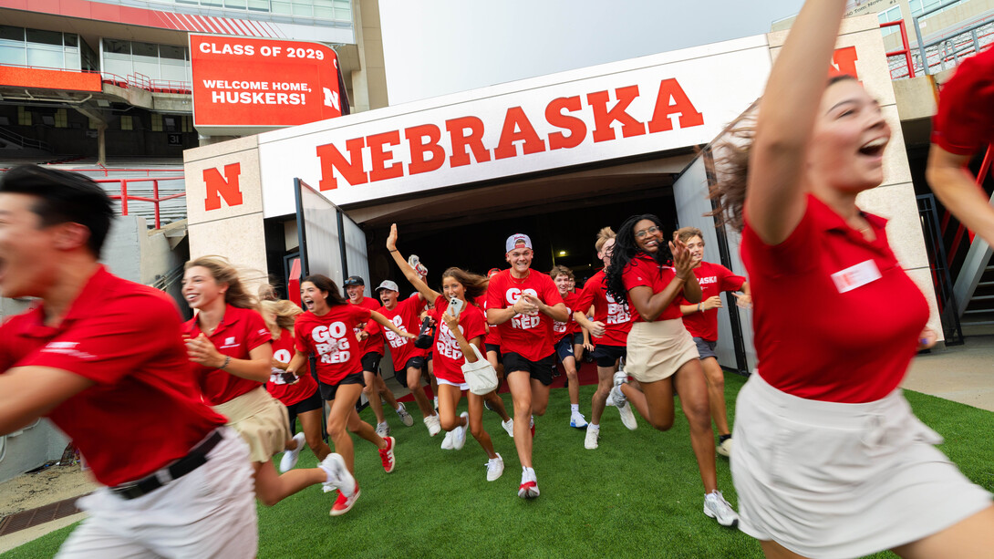 Students wearing red "Go Big Red" T-shirts run out of a tunnel at Memorial Stadium.