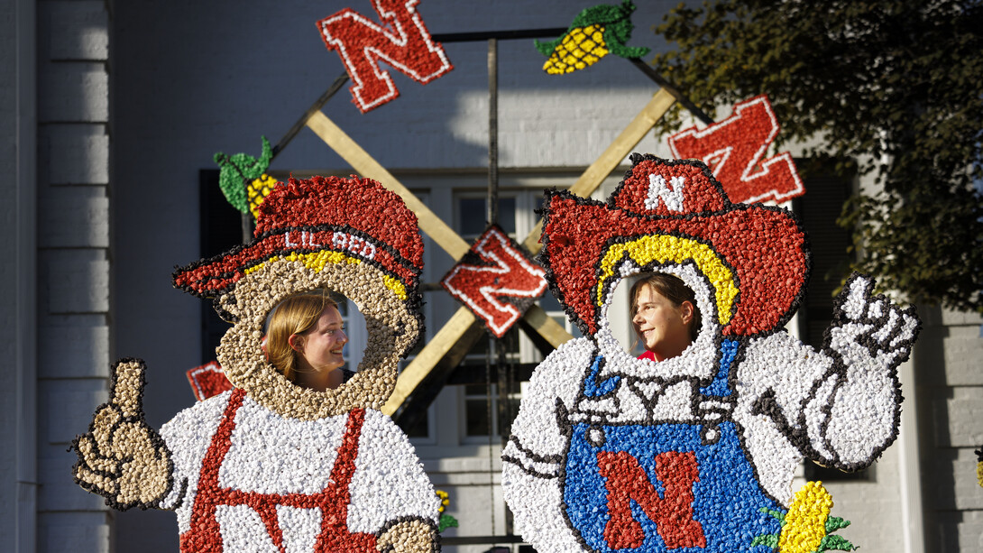 Two female students put their heads through Lil Red and Herbie cutouts decorated with pomping in front of a fraternity house.