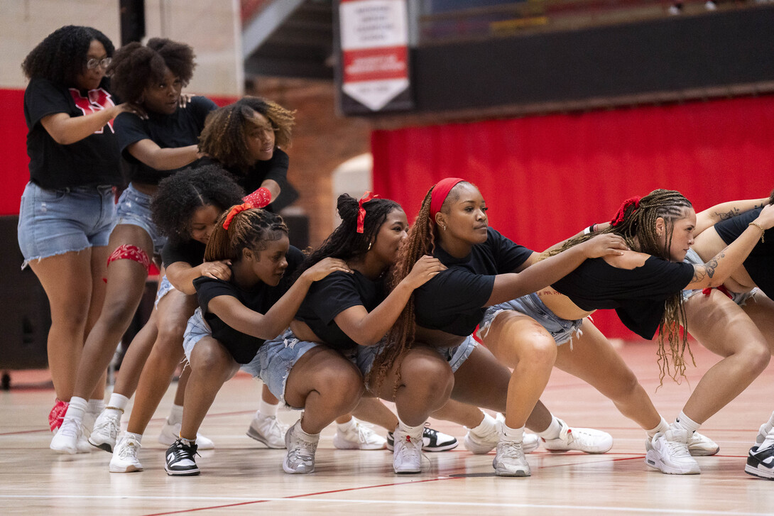 Ten young women representing the Afrikan People's Union dip down in a train formation on an athletic court.