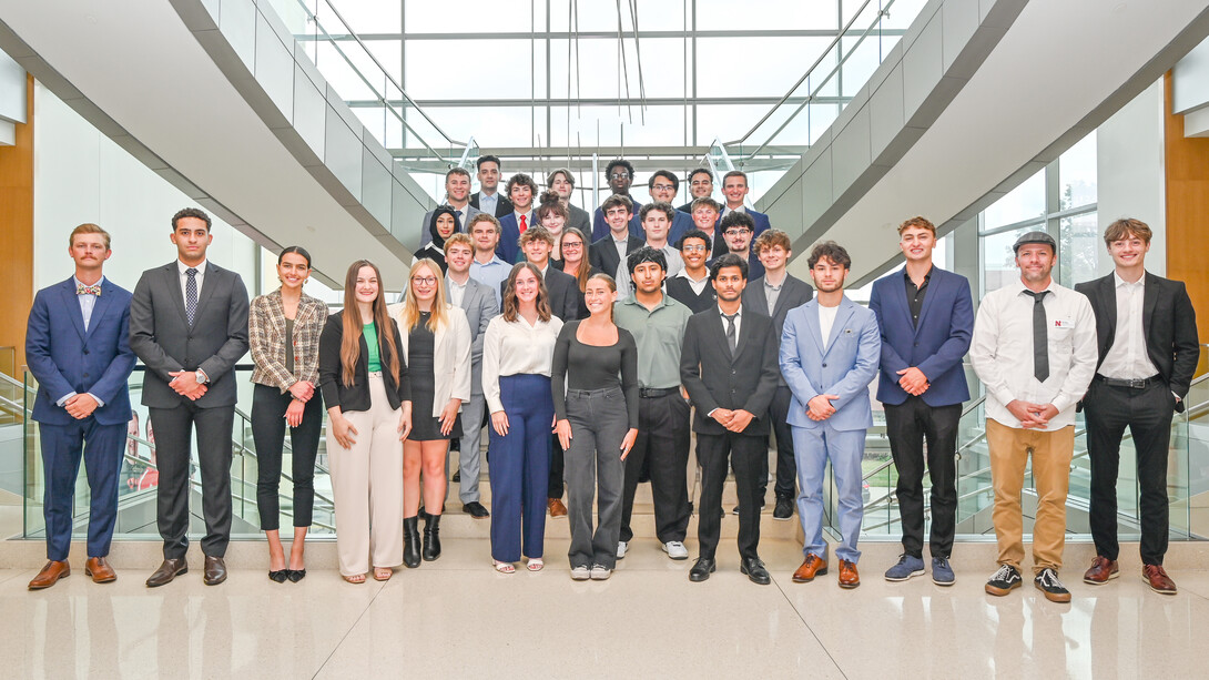 Thirty-three young people — all students in the Nebraska Entrepreneurship Accelerator — pose near a staircase in Howard L. Hawks Hall in formal attire.