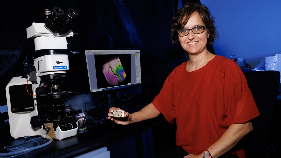 Lucia Fernandez-Ballester, assistant professor of mechanical and materials engineering, poses next to a microscope and computer monitor in a lab.