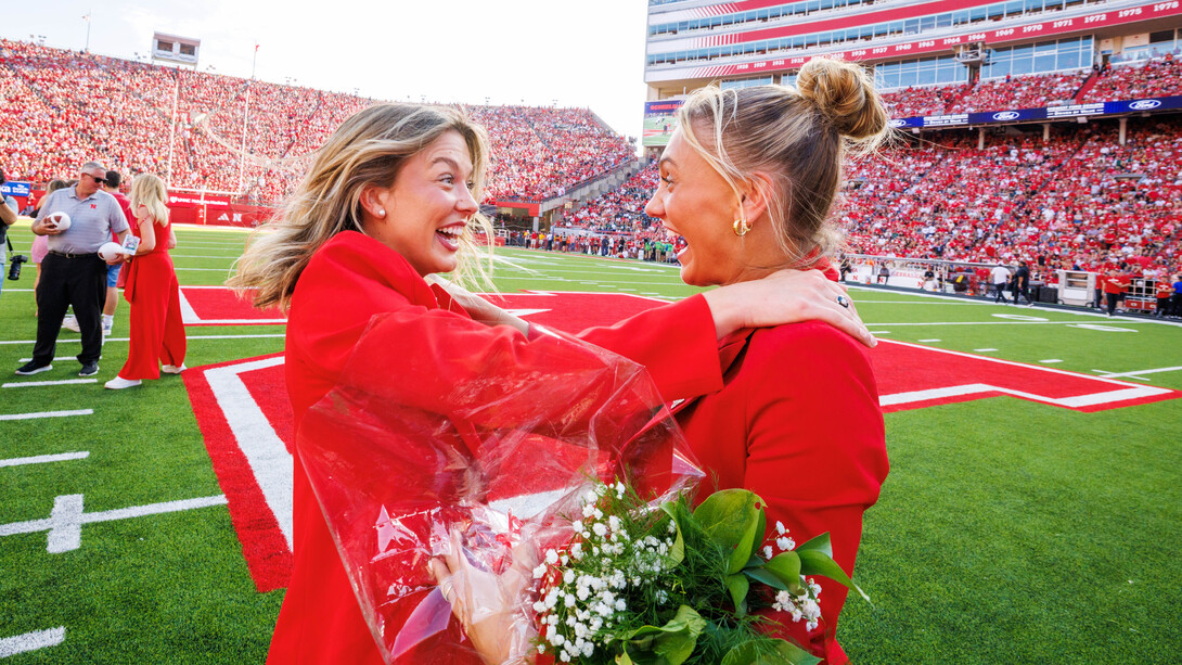 Homecoming royalty winners Claire Kelly (left) and Ava Hollingsworth, dressed in red and black formal attire, celebrate at midfield in Memorial Stadium.