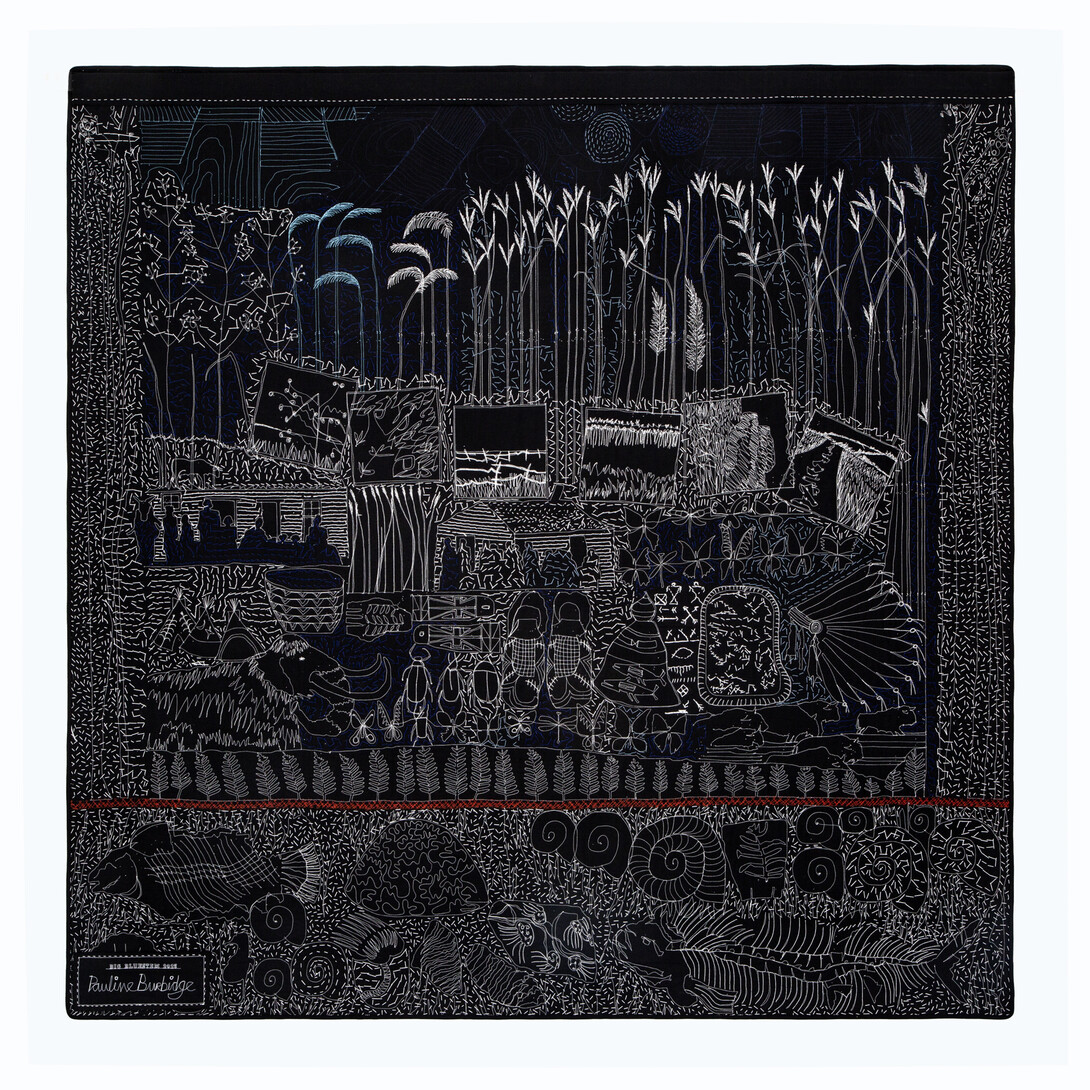 A black quilt backing with white stitches showing prairie grasses, a woolly mammoth, Native imagery and fossils.