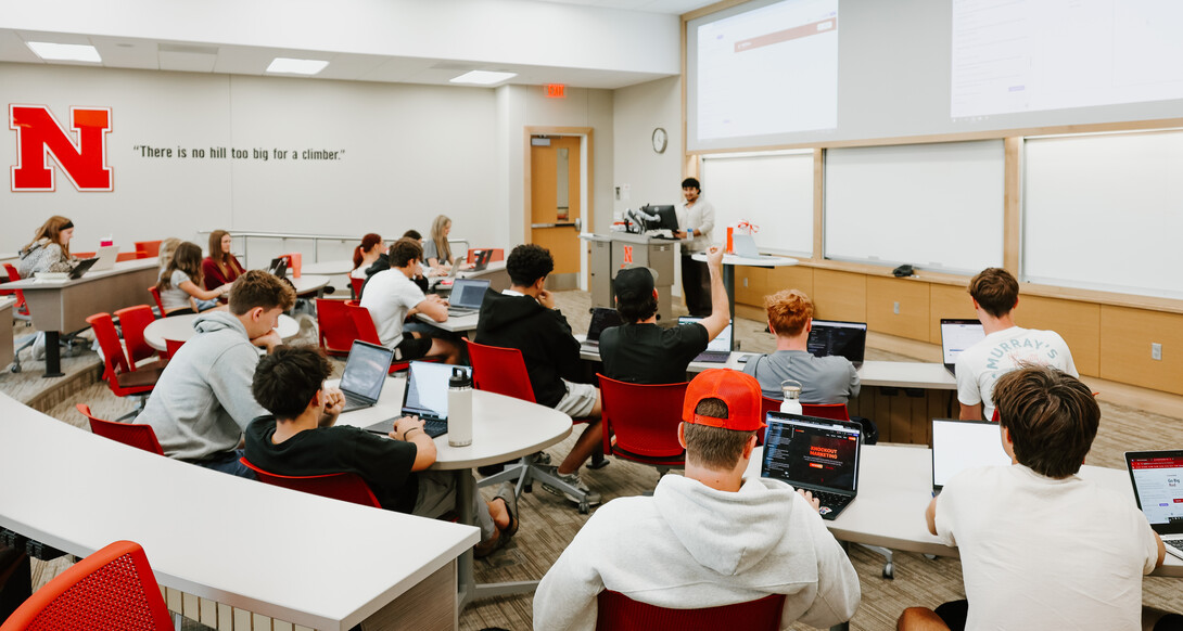 A young man speaks at a lectern to a class full of fellow students.