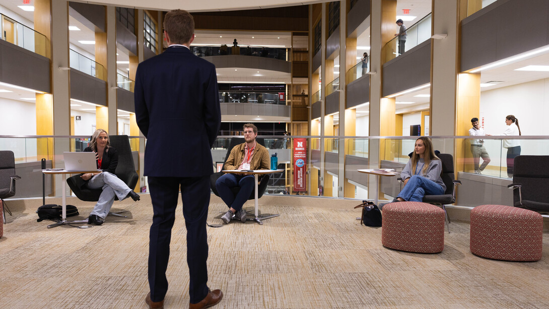 Gavin Dunlap, a sophomore finance major, stands in front of three judges near the atrium of Howard L. Hawks Hall. He is wearing a suit.