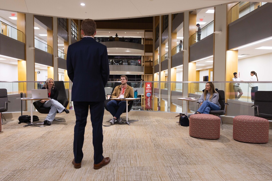 Gavin Dunlap, a sophomore finance major, stands in front of three judges near the atrium of Howard L. Hawks Hall. He is wearing a suit.