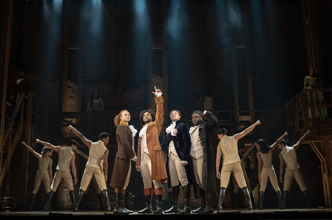 Four principal actors in Colonial-era costumes stand center stage with other cast members posing behind them in this publicity photo for "Hamilton."