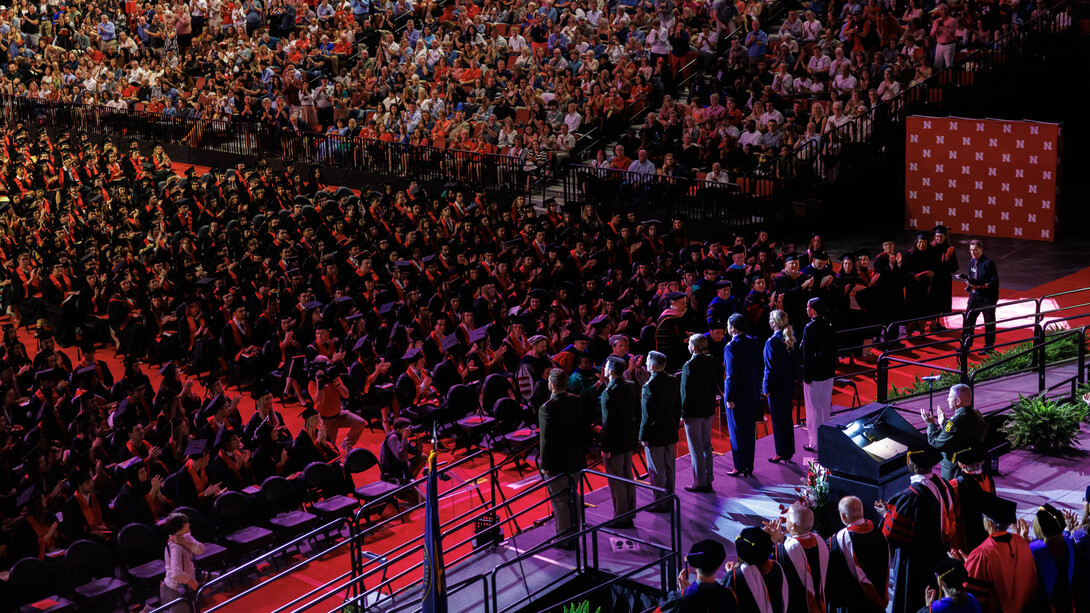 Seven ROTC members in uniform stand onstage at Pinnacle Bank Arena as the audience and their fellow graduates applaud.