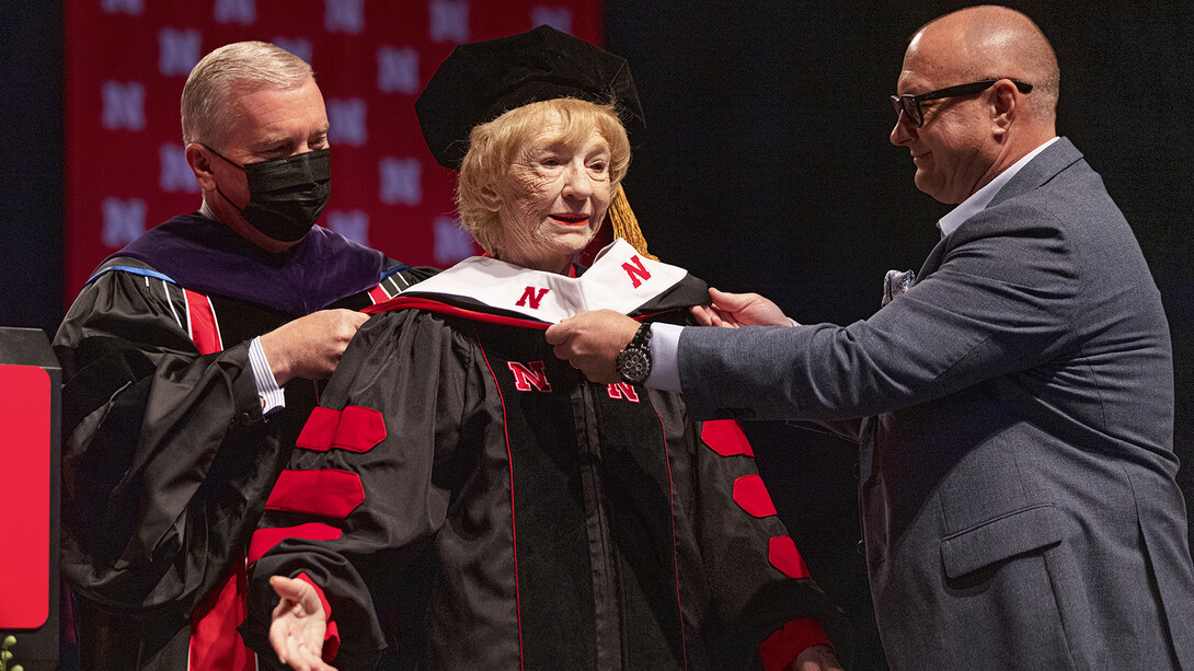 Leta Powell Drake spreads her arms as she is hooded by NU Regent Tim Clare and her son.