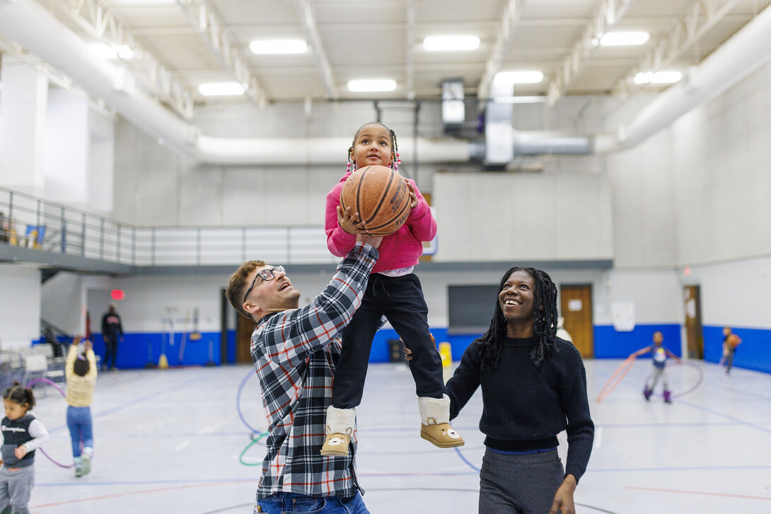 Ben Bentzinger, a senior in criminal justice, and Francisca Lawson Tettevie  a graduate student with CYAF, help Journey shoot a basket at the Malone Center.