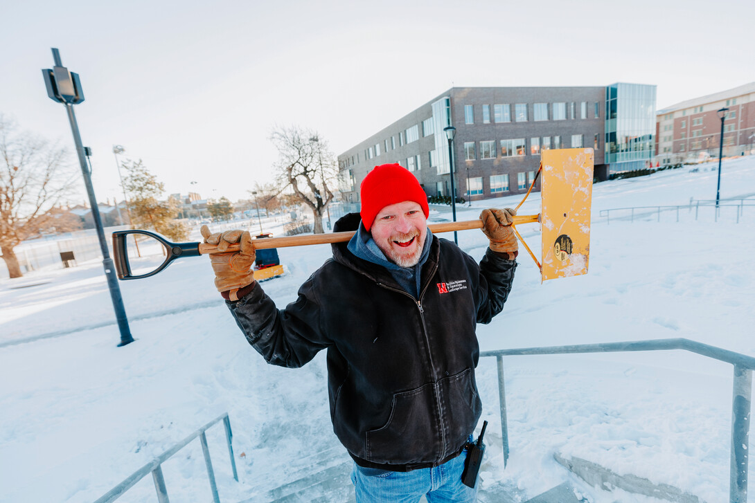 Kevin smiles for a photo while he holds a snow shovel across his shoulders