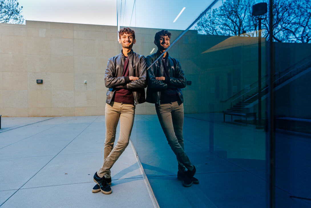 Aaryan Naik leans against Hawks Hall for a photo with his reflection in the glass of the building