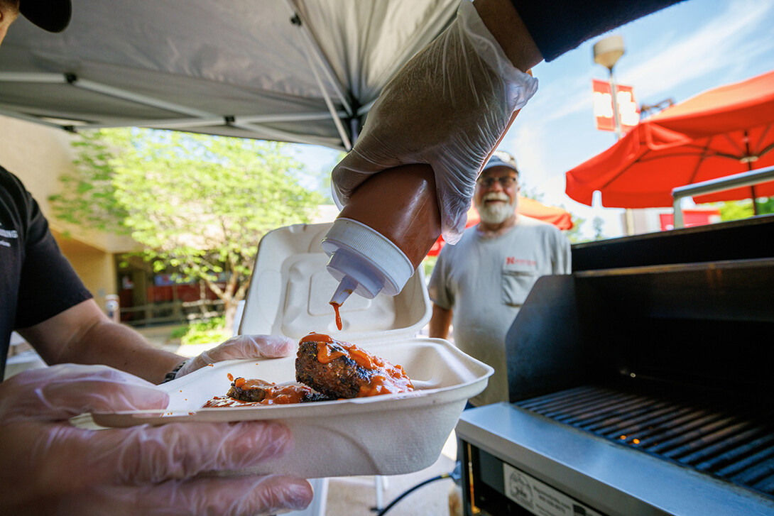 Sean Jones, a line cook with dining services, adds Oklahoma BBQ sauce to Jeff Logans order of ribs and sausages.