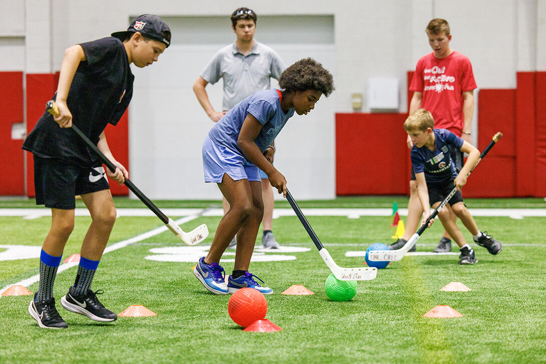Campers in a field hockey relay maneuver the ball around cones.