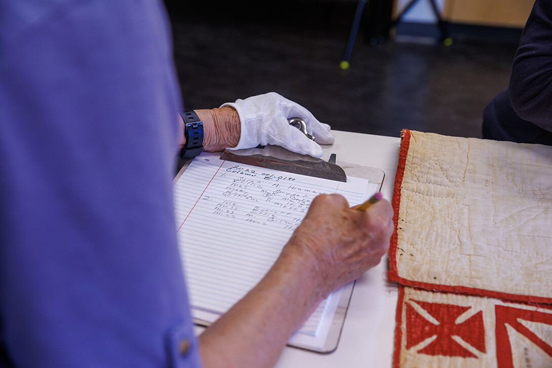 A woman writes on a clipboard next to a red and white quilt.