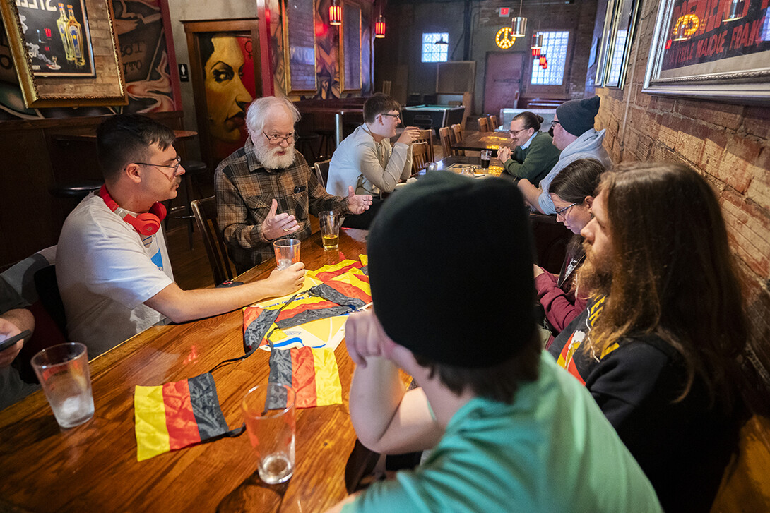 People talk while seated around a table decked with German flags.