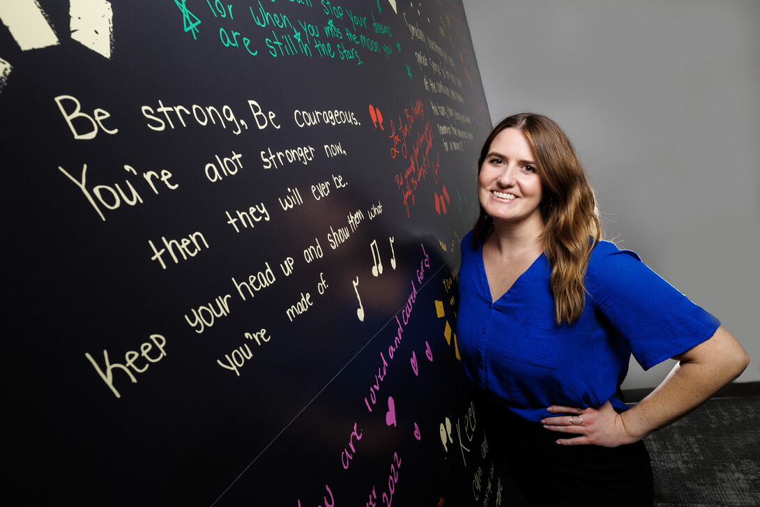 Gina May, Project SAFE clinical coordinator and graduate student, stands next to a wall containing inspirational messages inside the BraveBe Child Advocacy Center written by adolescent and teenaged clients.