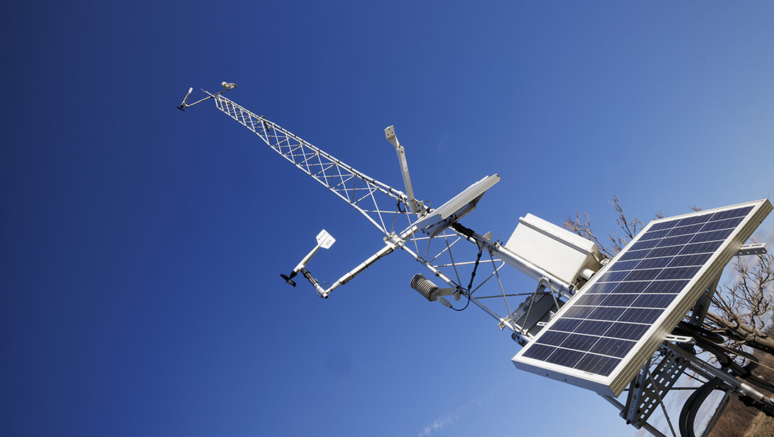 A Nebraska mesonet station rises into a blue sky on East Campus.