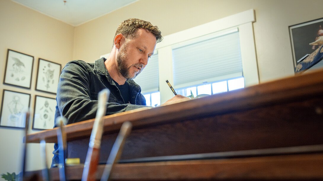 Scott McDonald draws at the desk in his home studio. McDonald works as a custodial manager on campus. He is also a self-taught artist.