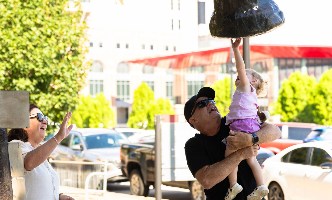 Greg Ferderer lifts his two-year-old granddaughter, Lexi, up to to Archie, the bronze mammoth statue in front of Morrill Hall. 
