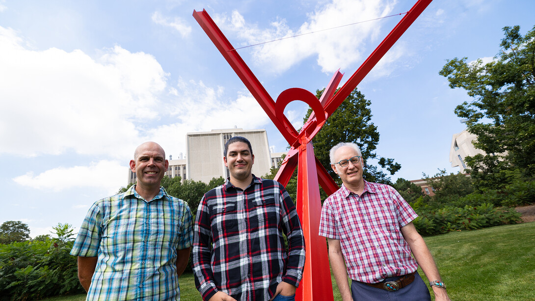 Three UNL researcher standing by the red steel beam sculpture, "Old Glory."