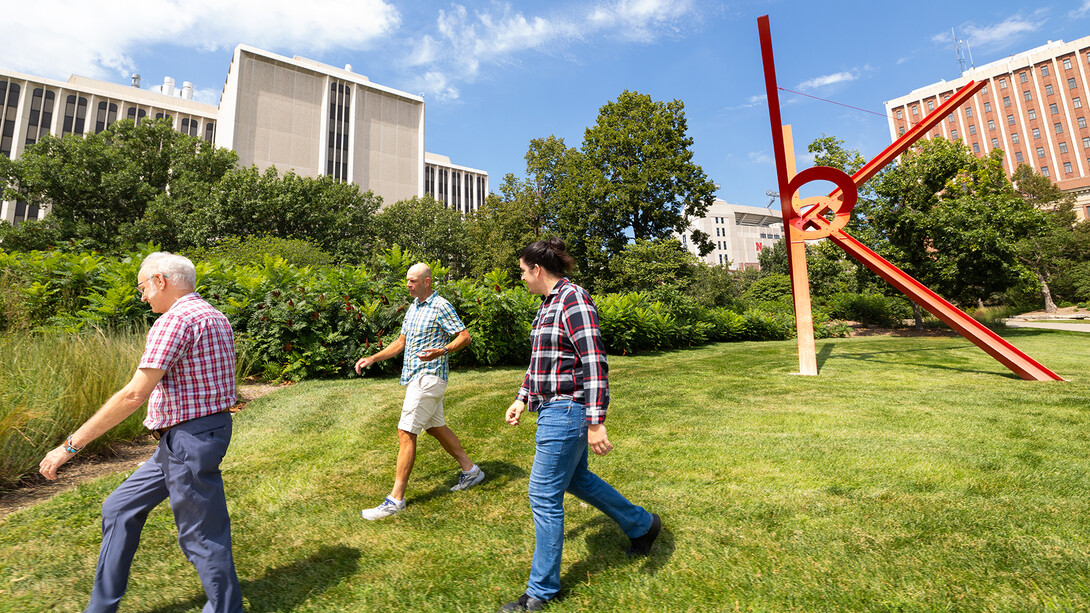 Three UNL researchers walking in grass next to the Old Glory sculpture.