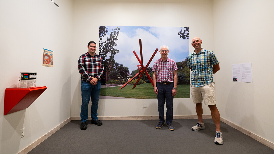 Three researchers standing by a Sheldon Museum of Art exhibit on the "Old Glory" sculpture.