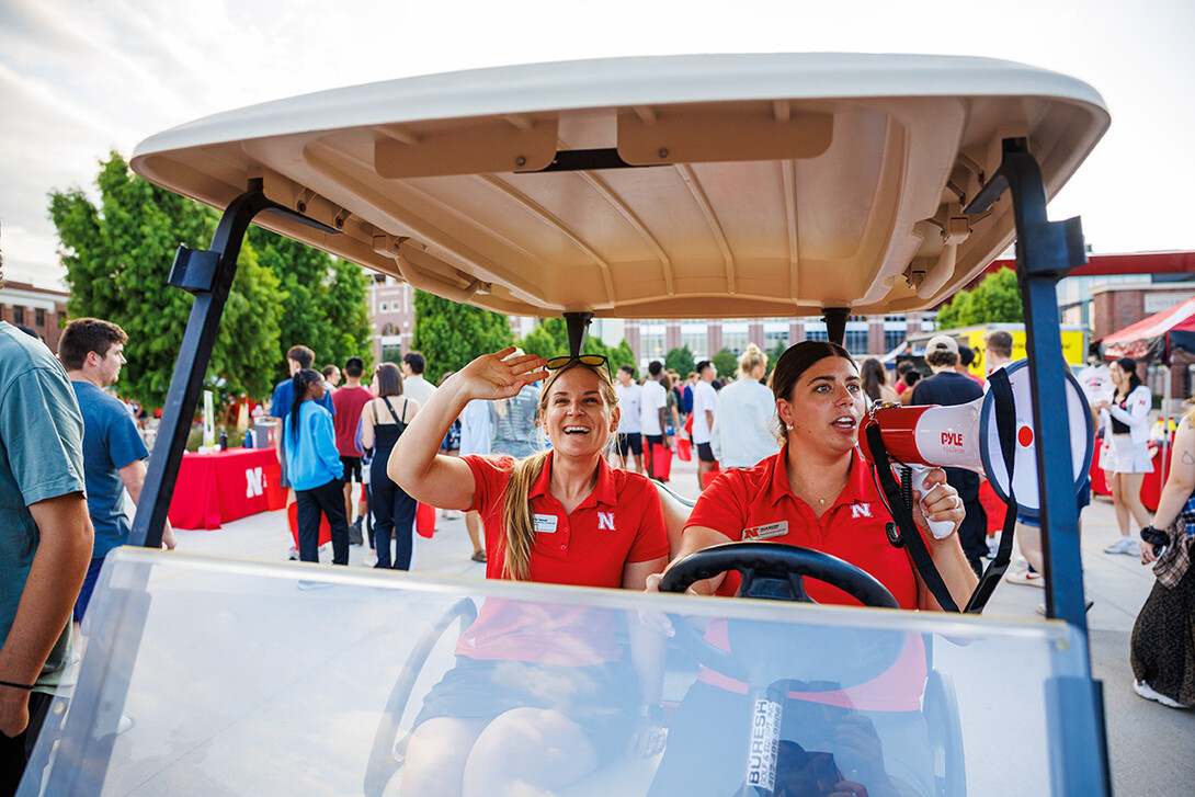 Hollie Swanson and Kalan Walters drive a golf cart through the Street Festival of Big Red Welcome. Swanson and Walters helped plan this event.