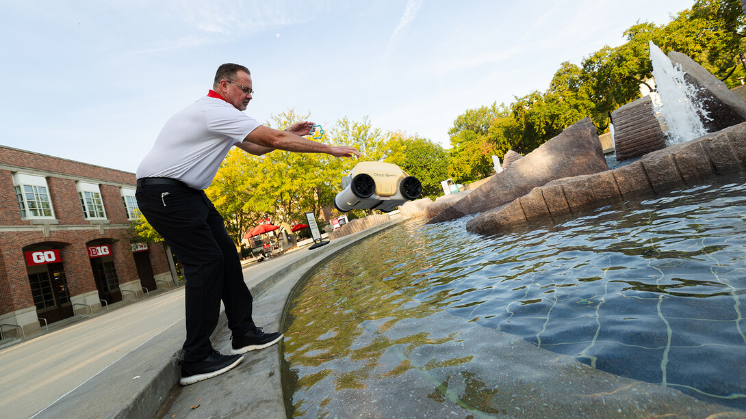 John Jenkin, facilities manager, tosses a robotic pool skimmer into Broyhill Fountain. The device helps keep the iconic campus fountain clean, collecting debris from the water.