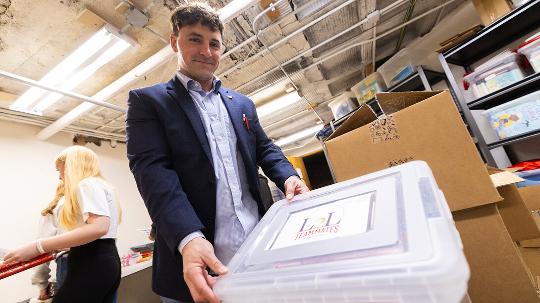 Ben Bentzinger holds up a box lid bearing the Linked2Literacy and TeamMates logos. As a Volunteer Ambassador, he partners with both groups to support mentoring and literacy efforts in Lincoln.