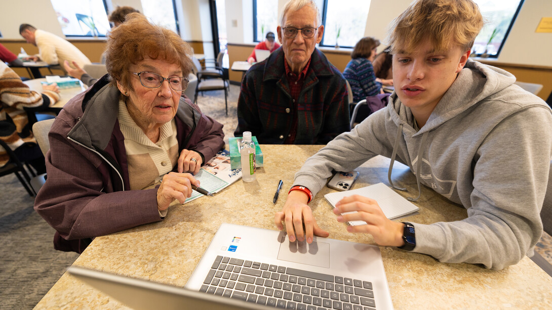 Three people sit around a table as one navigates a laptop desktop.