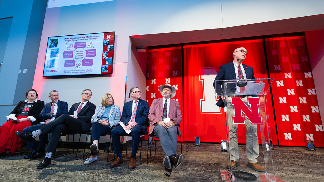 Thomas Burkey, interim dean of the College of Agricultural Sciences and Natural Resources, steps up to the podium during the University of Nebraska–Lincoln's Charter Day event, with deans representing the Nebraska Extension, research, the Colleges of Business, Law, and Education & Human Sciences, and Libraries lined up to speak.