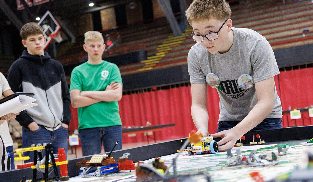 Some students look on as another student runs a practice match with a LEGO robot.