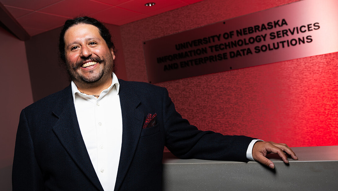 Raul Ochoa stands in front of a sign that reads University of Nebraska Information Technology Services.