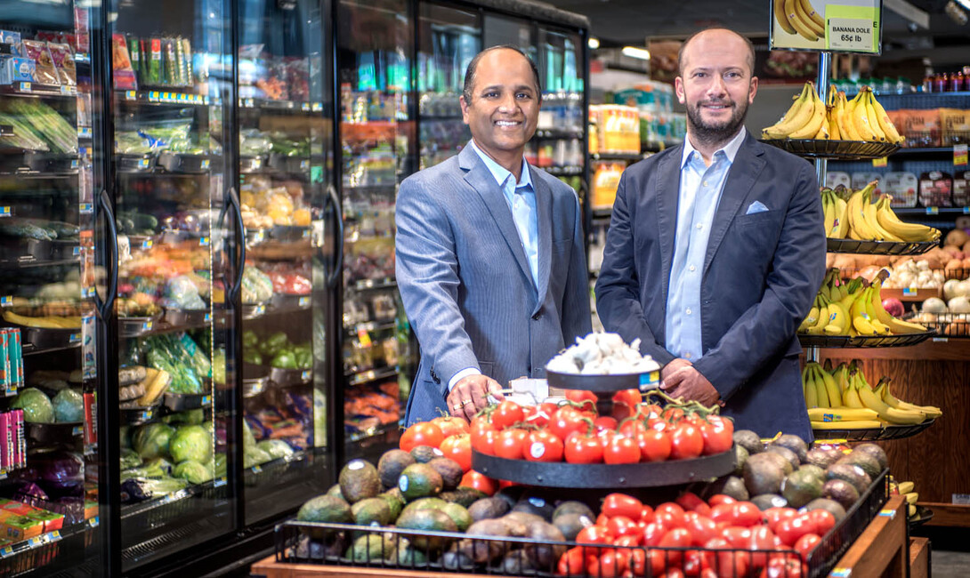 S. Sajeesh and Özgür Araz are photographed in a produce section of a grocery store.