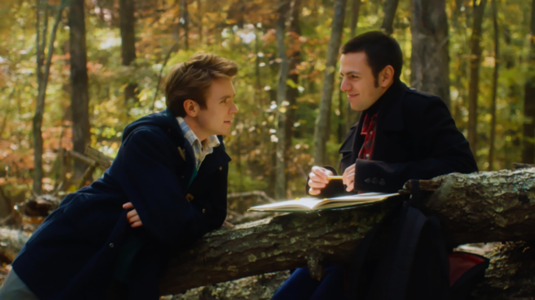 A film still from "Before We Forget" shows two men smiling in a forest.