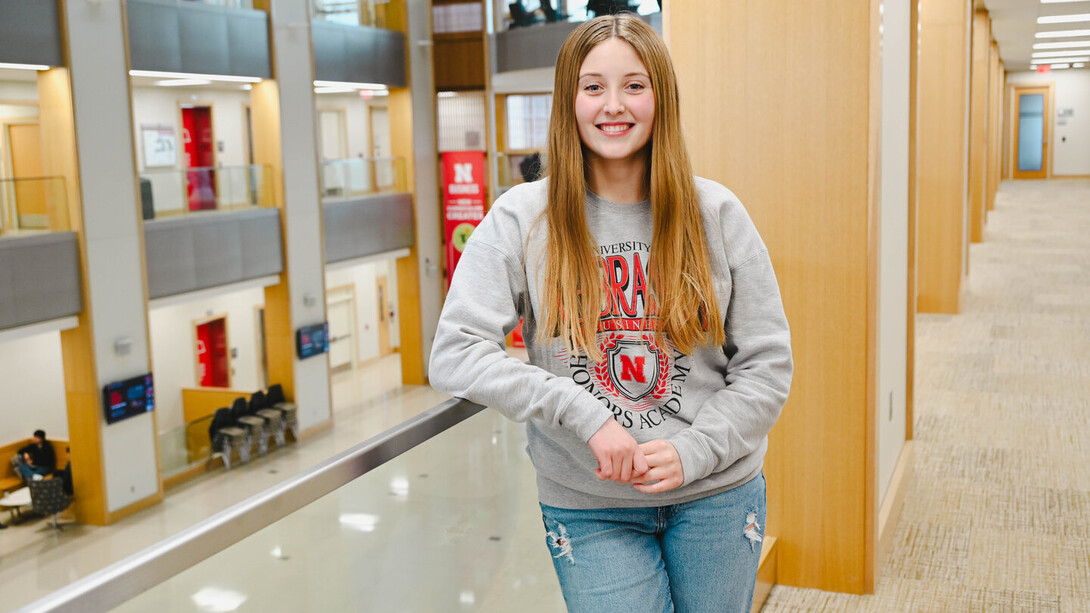 Maci Dorshorst stands in a grey and red Nebraska long sleeve shirt and jeans, her long blonde auburn hair covering her ears.