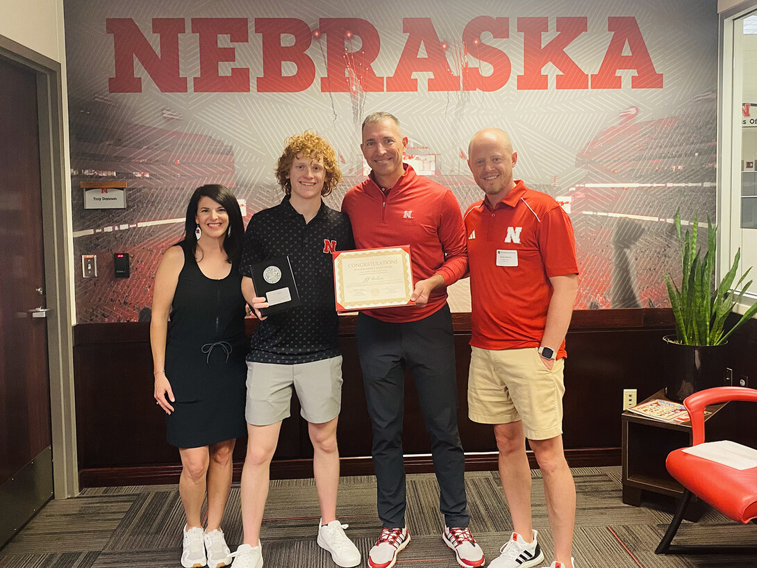 Presidential Scholar Jeremy Robson and his parents, Jeremy and Kelly, stand with Chris Kabourek, interim NU president, in front of a wall that shows Memorial Stadium and a "Nebraska" banner.