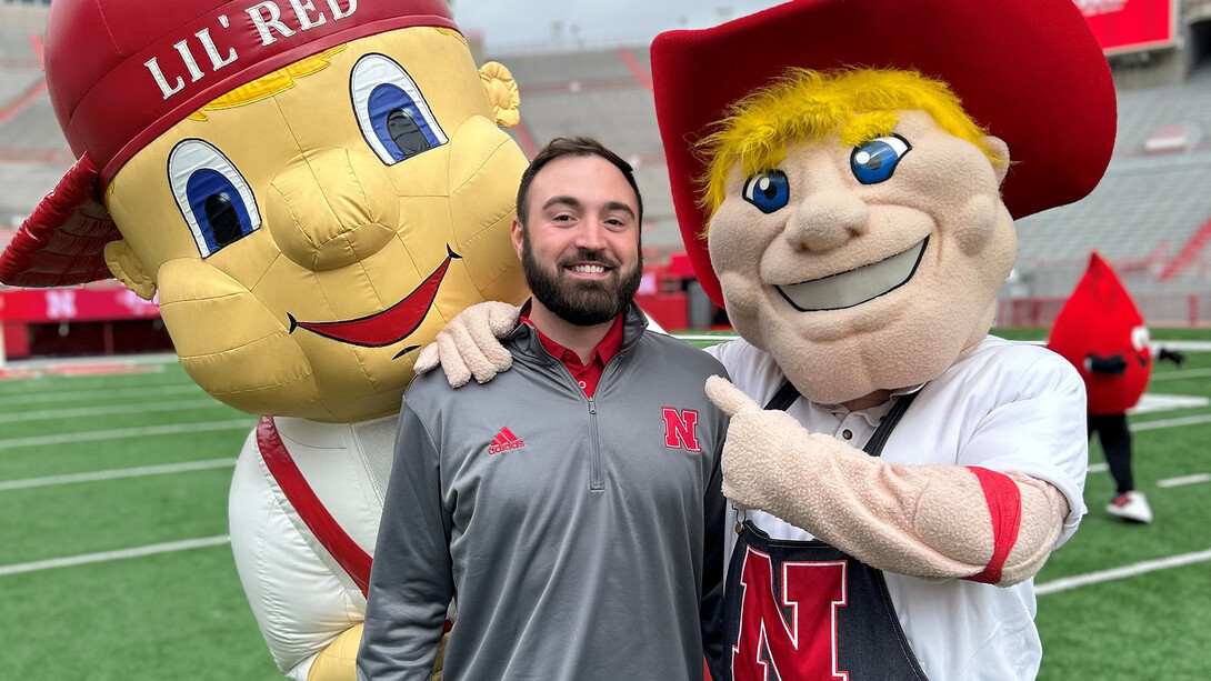 Connor O'Dell posing with Herbie Husker and Lil' Red on the turf in Memorial Stadium.