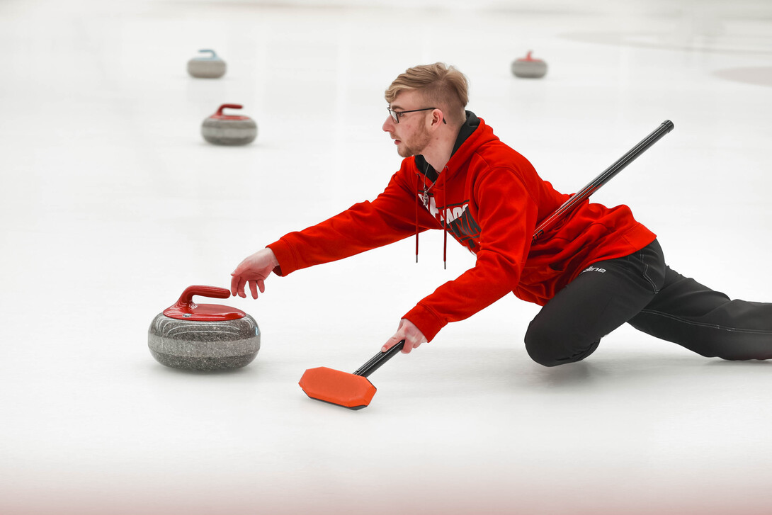 Brett Johnson slides a curling stone Saturday during the club team's bonspiel at the Breslow Hockey Center.