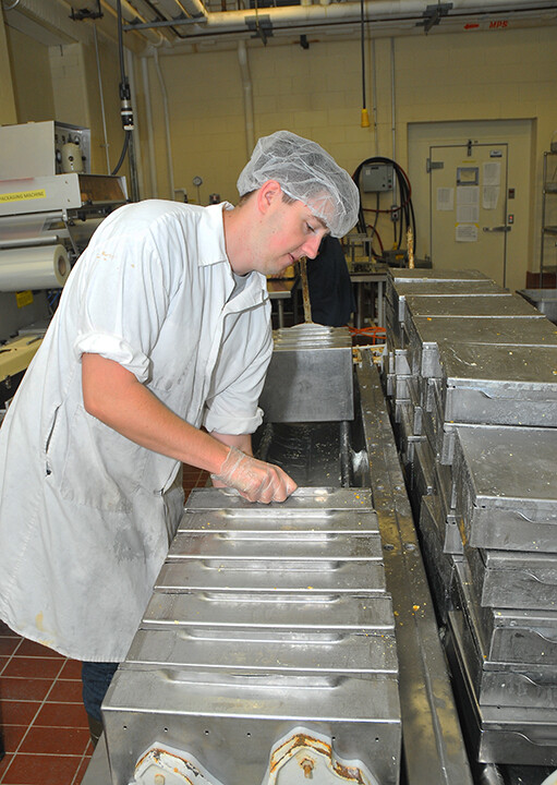Andrew Donovan, a student employee at the UNL Dairy Store, removes aluminum containers filled with 25-pound blocks of cheese.