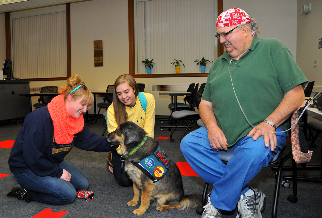 UNL students (from left) Lauren Martin and Laura Kowalski pet Boo, a Healing Hearts Therapy Dog, in Love Library on Oct. 15. Boo is a therapy and service dog owned by Gary Royal (right).