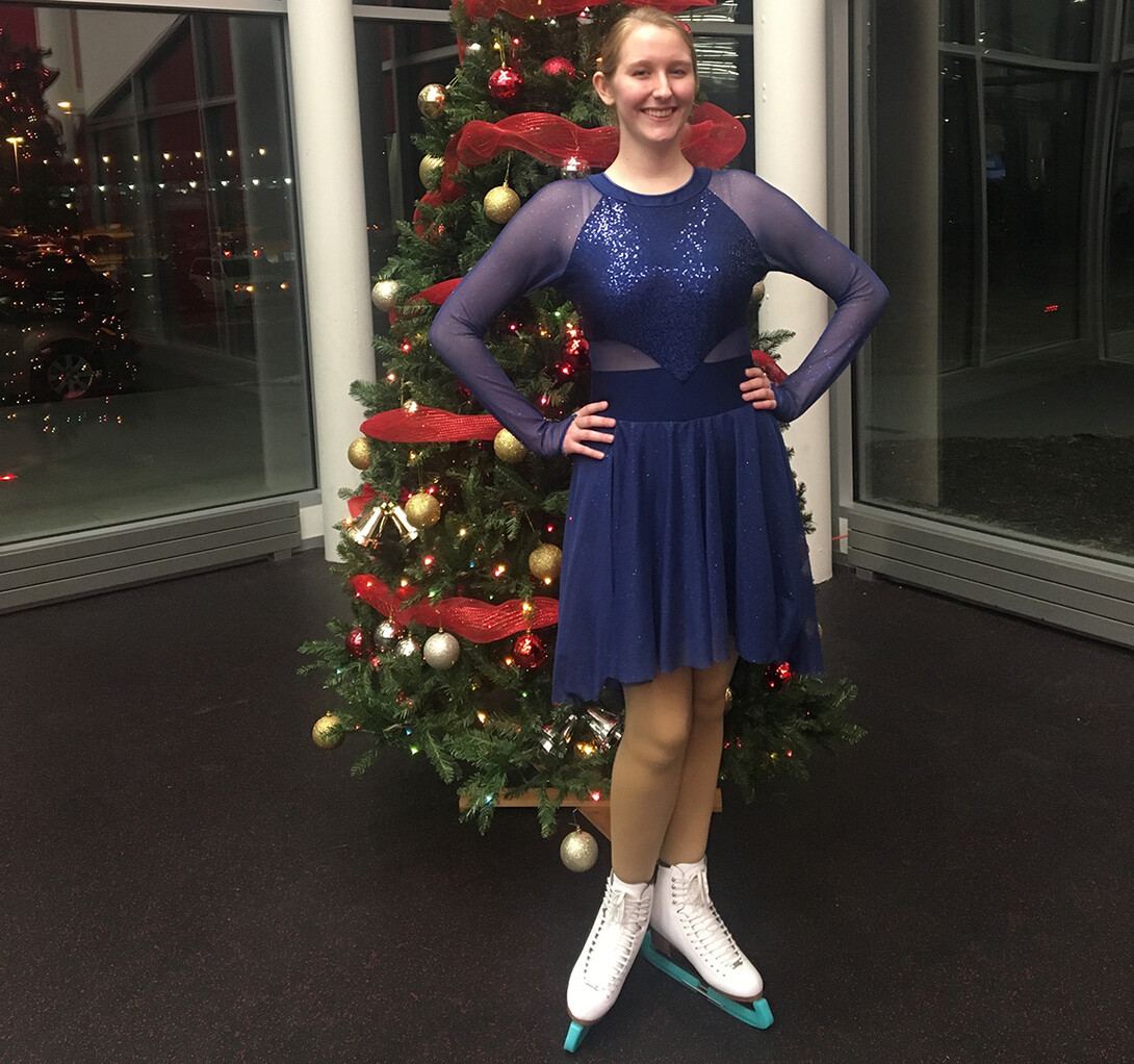Emma Dolenshek stands in front of a Christmas tree while wearing a synchronized ice skating outfit and skates. She has recently gotten back into the sport following an injury and the pandemic.