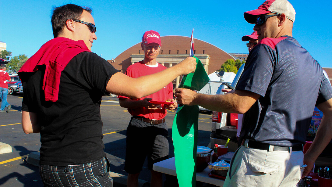 A Go Green for Big Red volunteer (left) hands out a green bag to collect tailgating recyclables during Nebraska's 2018 football season. The recycling program begins its 11th season on Aug. 31.