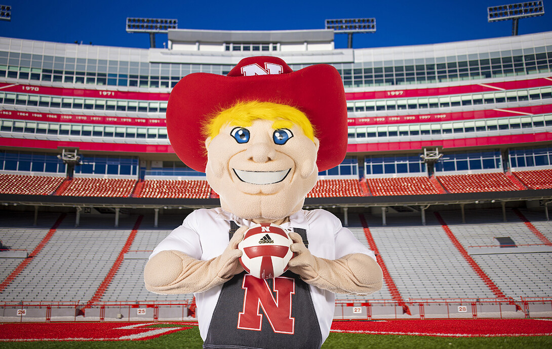 Herbie Husker stands in Memorial Stadium holding a volleyball.